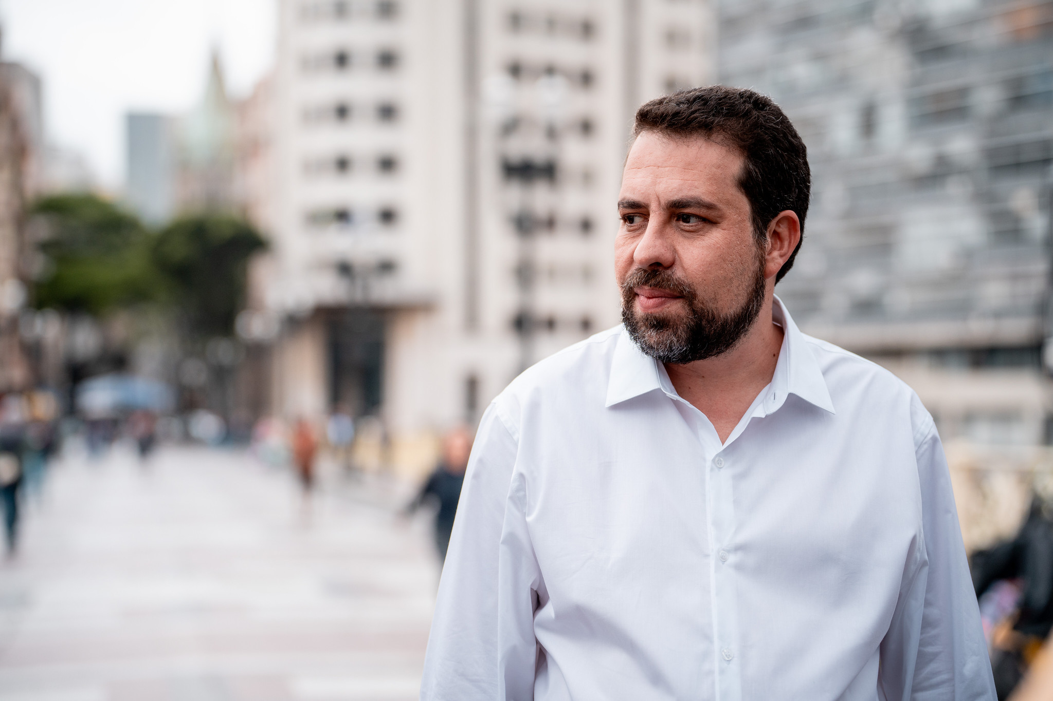 Guilherme Boulos (PSOL) com expressão serena, olhando para o lado, vestindo camisa social branca