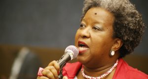 Macaé Evaristo (PT-MG), nova ministra dos Direitos Humanos, de roupa vermelha, de perfil, falando em microfone, séria
