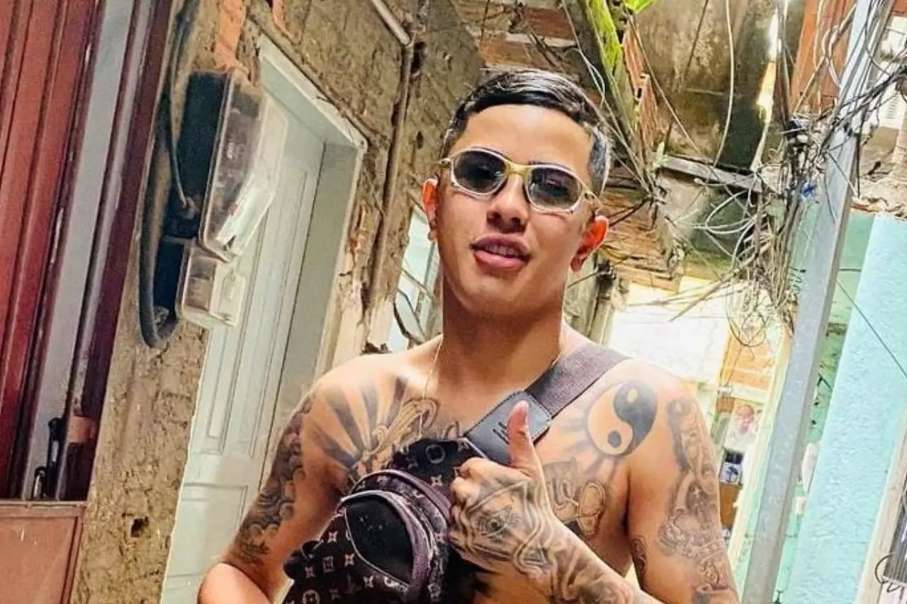 MC Vini VL sem camisa, com pochete e óculos escuros, posando e gesticulando para foto
