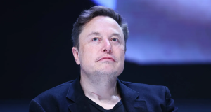 Elon Musk de roupa preta, olhando para cima, sério