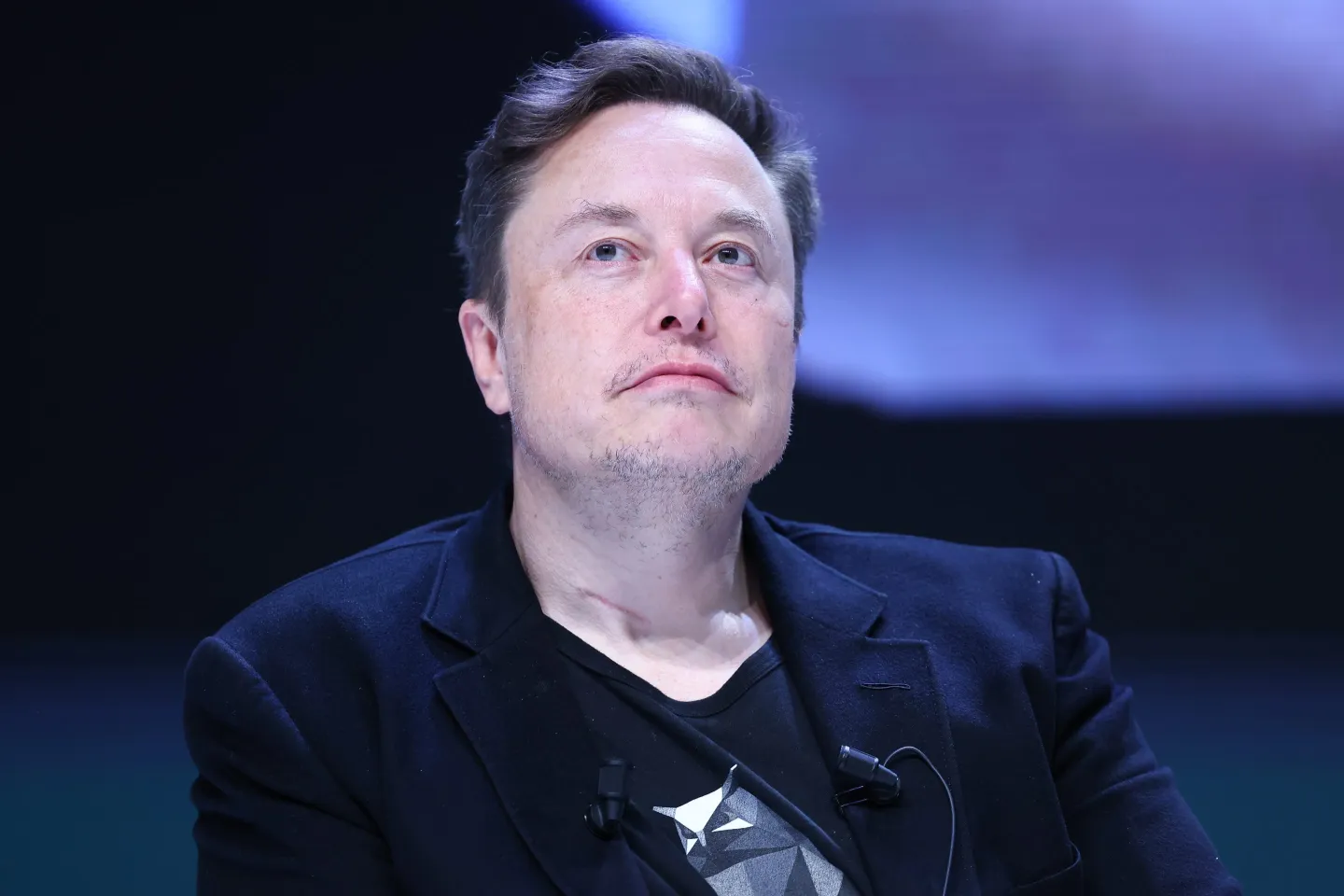 Elon Musk de roupa preta, olhando para cima, sério