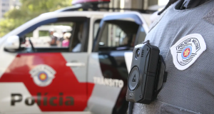 Carro da PM de SP ao fundo e agente em primeiro plano sem mostrar o rosto
