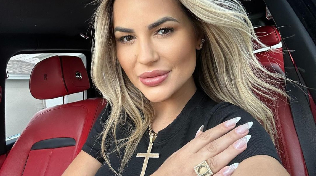 influenciadora Deolane Bezerra de cabelo solto e roupa preta, posando dentro de carro, séria