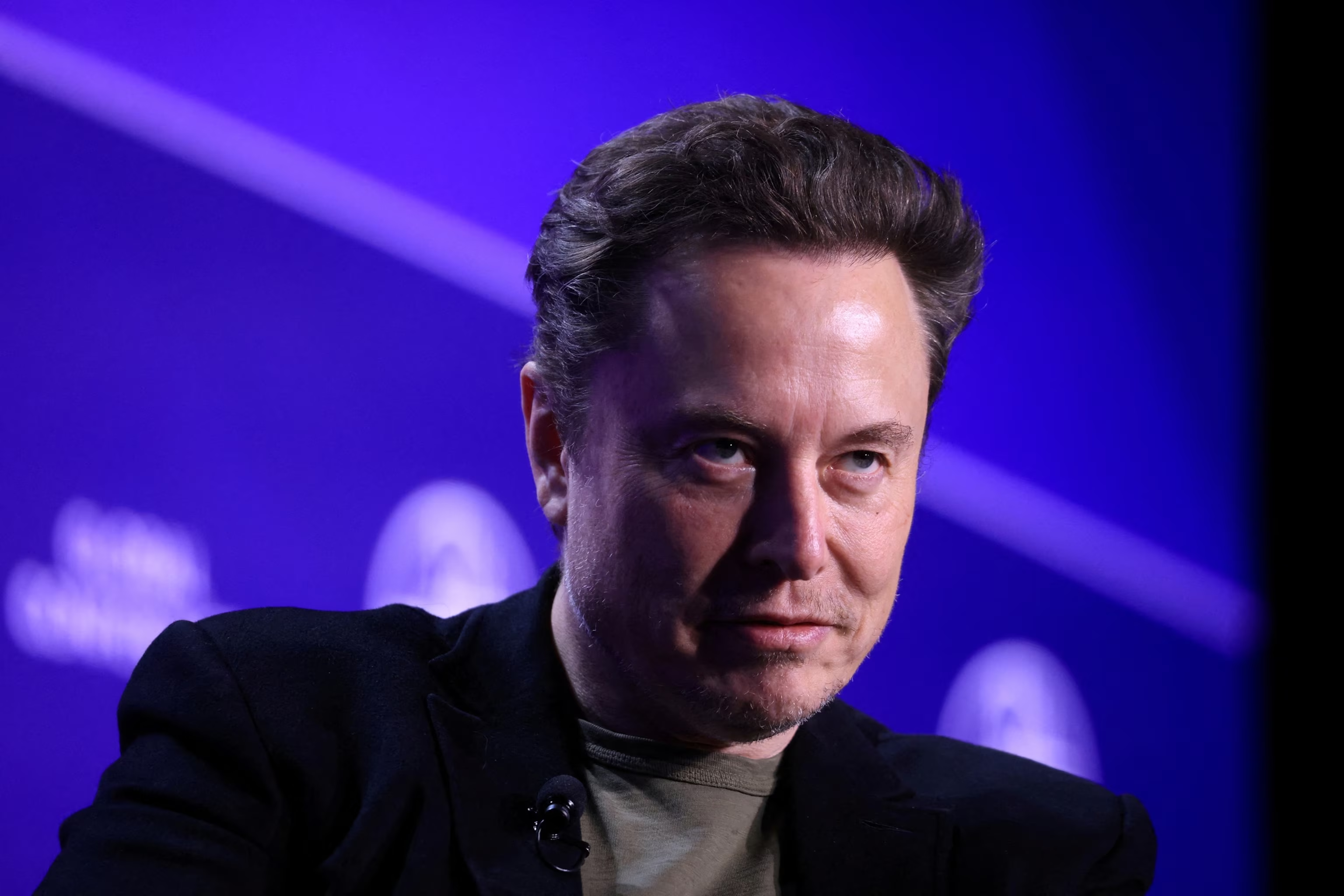 Elon Musk com expressão sugestiva, sem olhar para a câmera