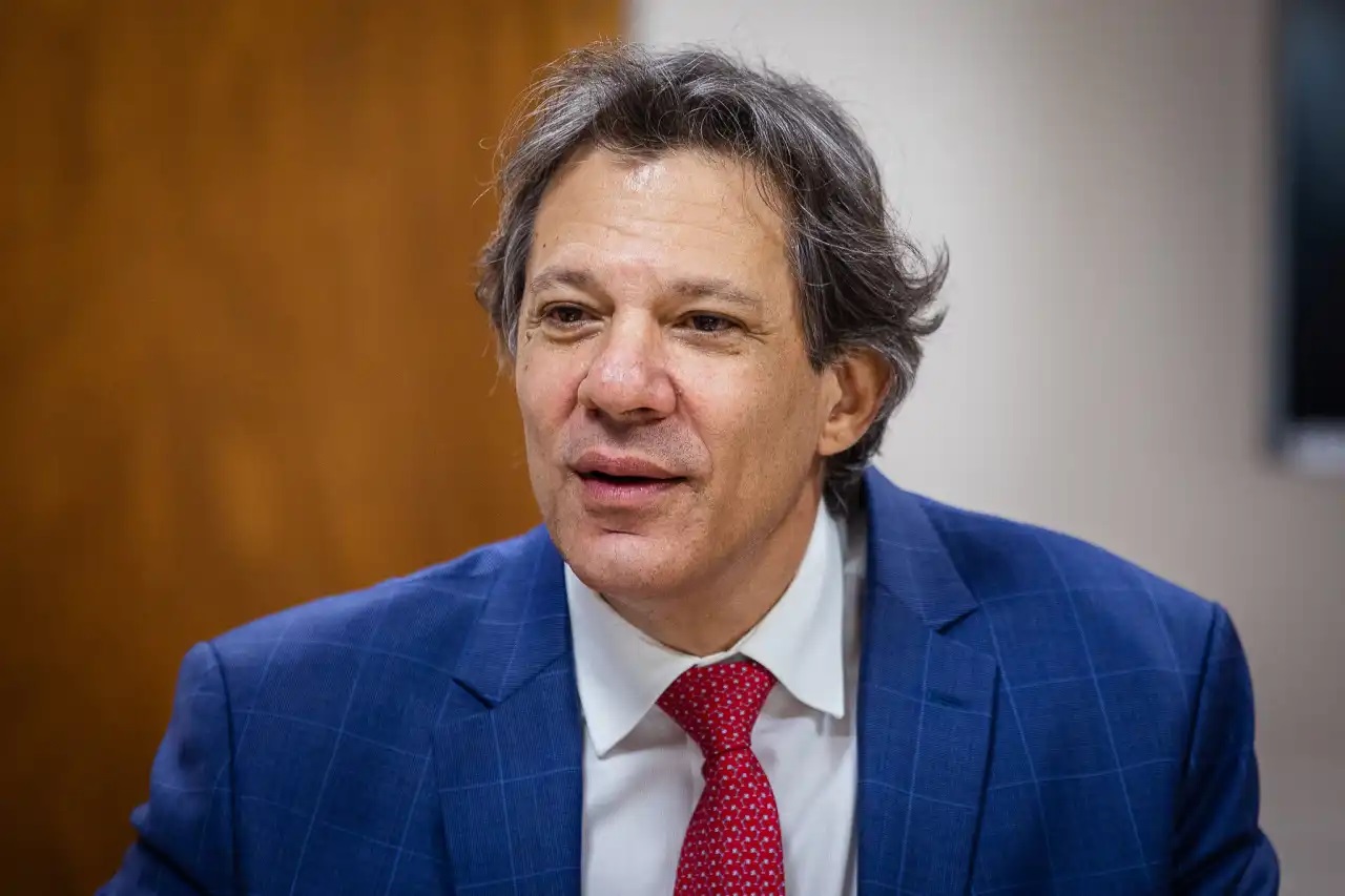 Fernando Haddad sorrindo de maneira tímida sem olhar para a câmera