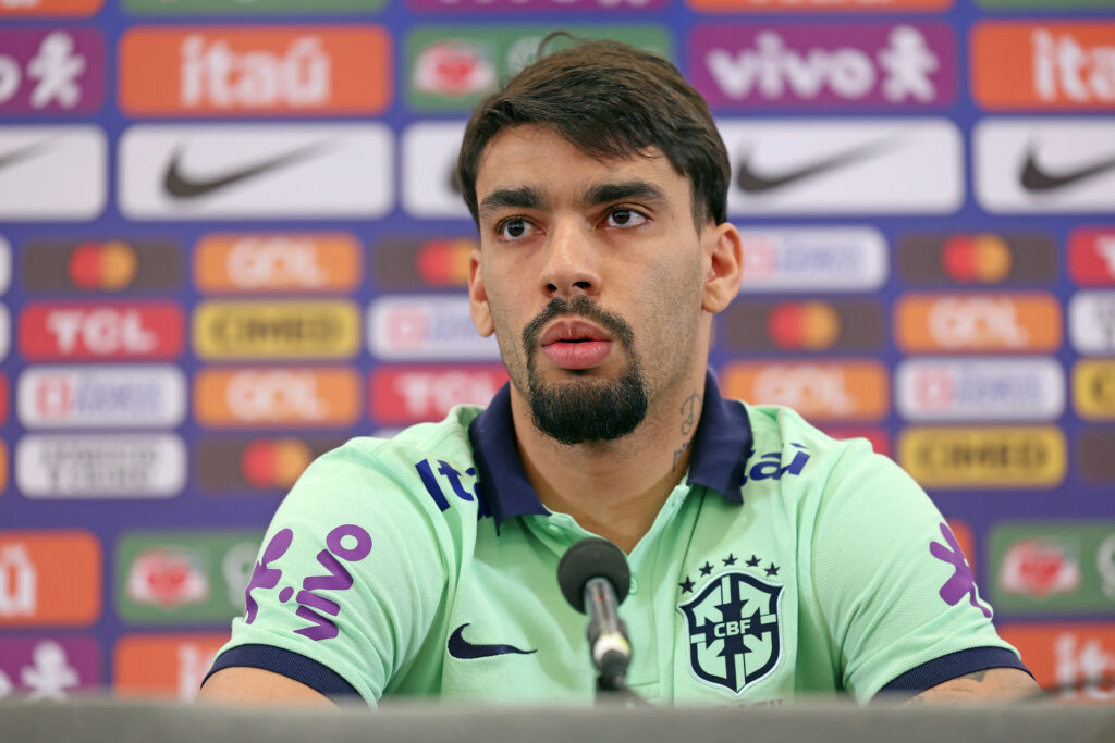 O jogador de futebol Lucas Paquetá sério, com camisa da CBF, olhando para o lado, em espaço de coletiva