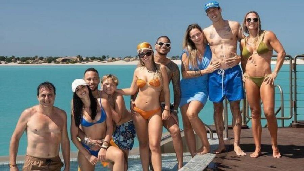 Neymar posando com familiares e amigos em pé, todos com roupas de banho, na praia