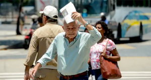 Idoso caminhando na rua e tentando se proteger do calor com jornal