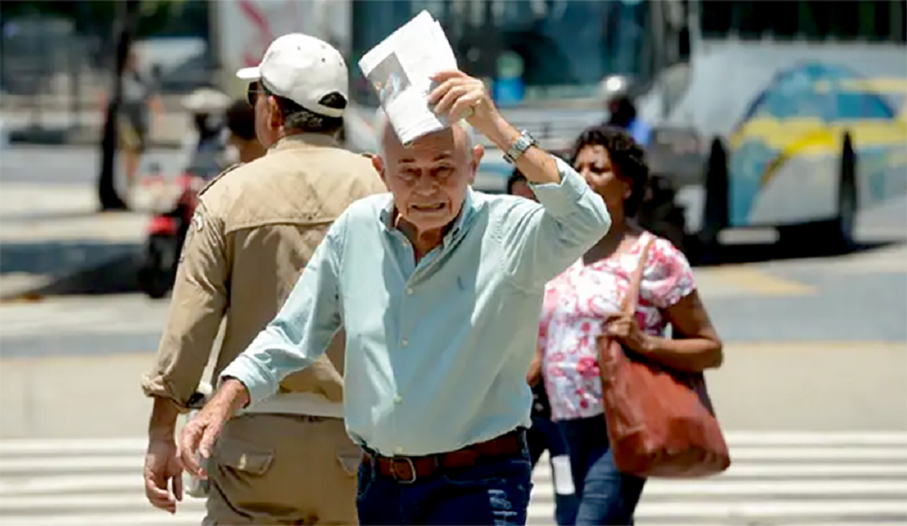 Idoso caminhando na rua e tentando se proteger do calor com jornal