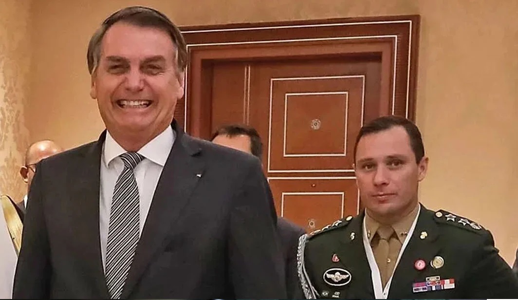 Jair Bolsonaro sorrindo ao lado de Mauro Cid sério