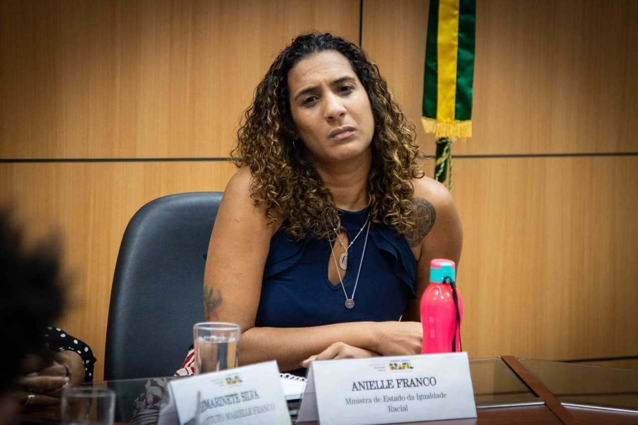 Anielle Franco de cabelo solto e camiseta azul marinho, com expressão de tédio