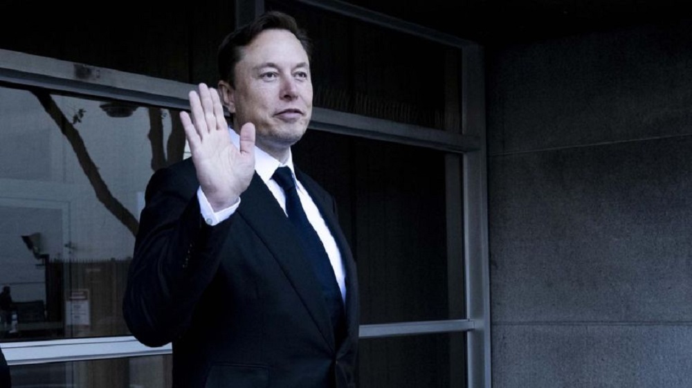 Elon Musk acenando, sério, sem olhar para a câmera