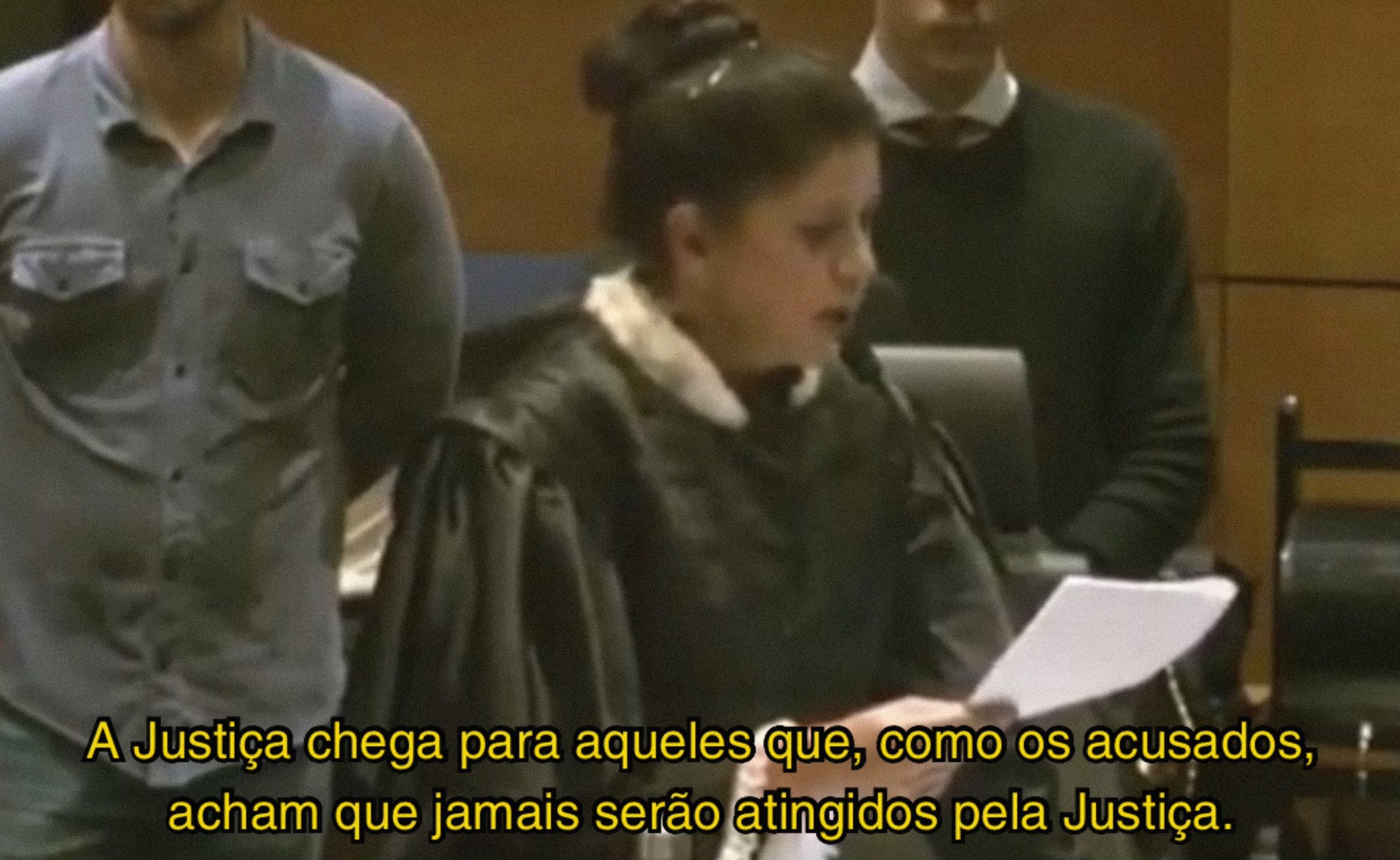 juíza Lúcia Glioche de cabelo preso, em pé, de perfil, lendo papel em microfone