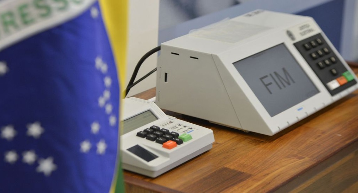 Urna eletrônica perto de bandeira do Brasil