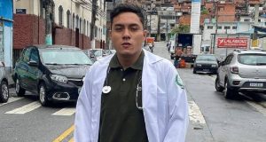 Marco Aurélio Cardenas Acosta de jaleco e camisa verde, sério, posando na rua com estetoscópio