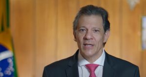 O ministro da Fazenda, Fernando Haddad, falando para a câmera, de terno e gravata, sério
