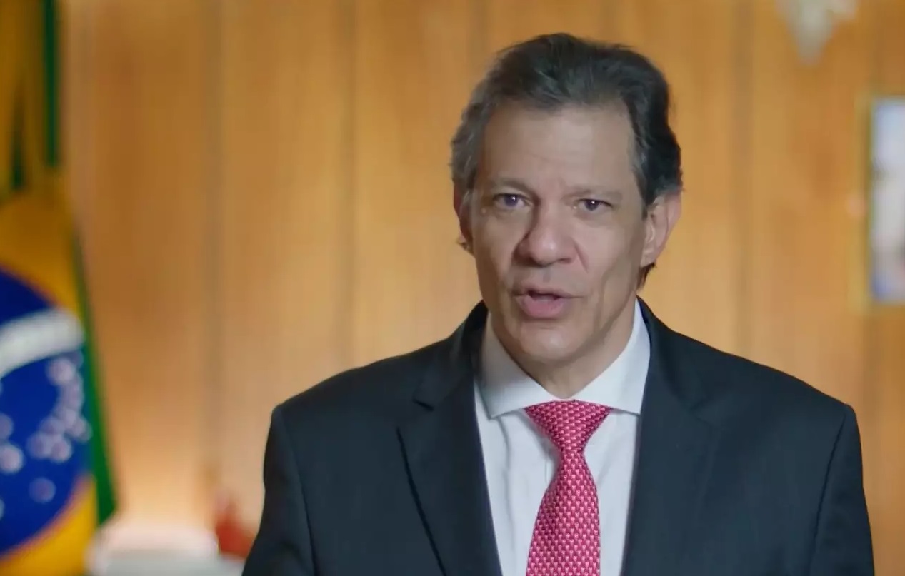 O ministro da Fazenda, Fernando Haddad, falando para a câmera, de terno e gravata, sério