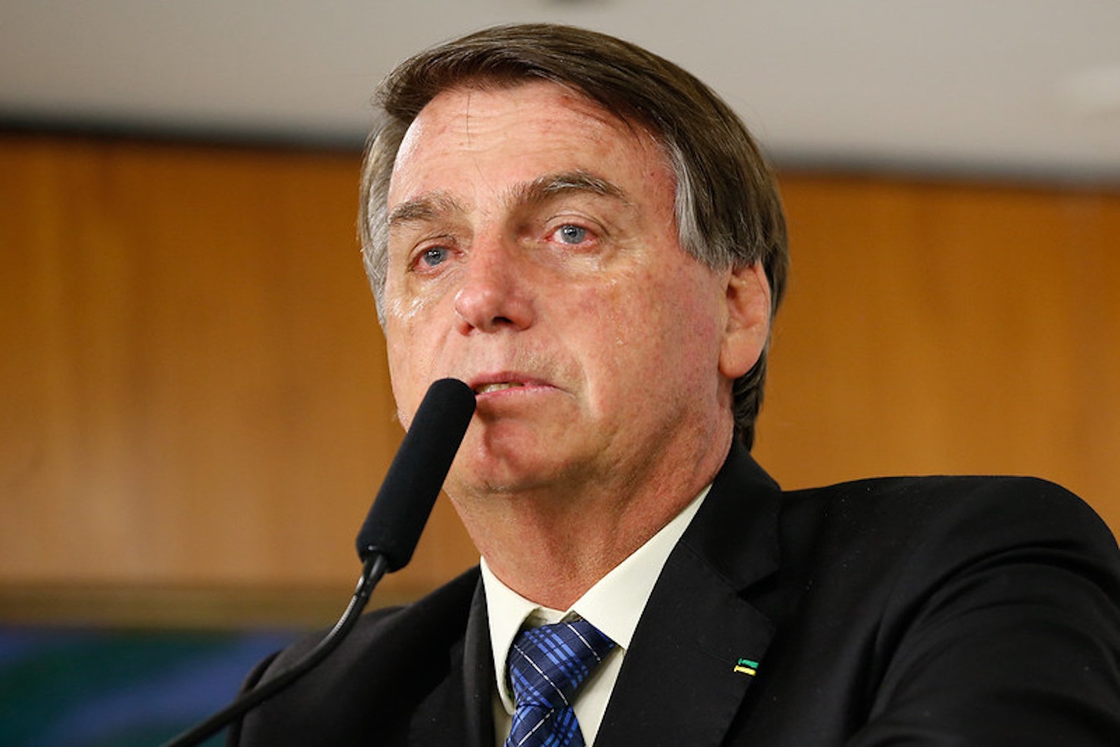 Jair Bolsonaro olhando pra frente com cara de choro, sem olhar para a câmera, perto de microfone