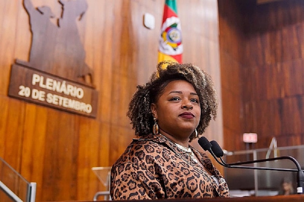 deputada estadual Bruna Rodrigues (PCdoB-RS) séria, de roupa de oncinha, perto de microfone, sem olhar para a câmera