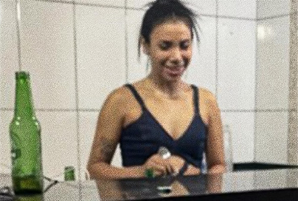 A cabeleireira Suziele Gomes de Oliveira de camiseta preta e cabelo preso, rindo e olhando para baixo