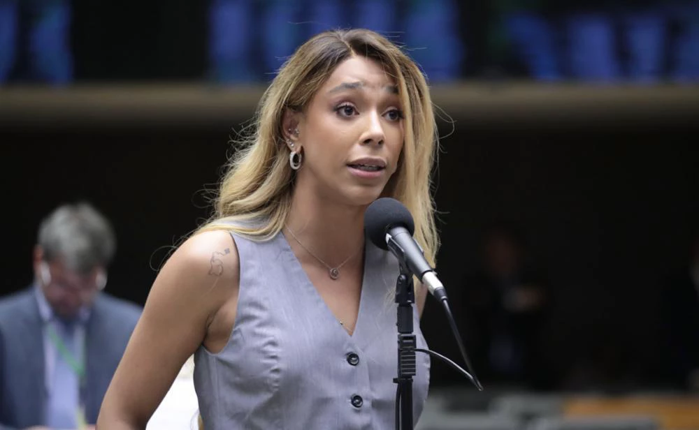 deputada federal Erika Hilton (PSOL) de roupa cinza sem mangas e cabelo solto, falando em microfone