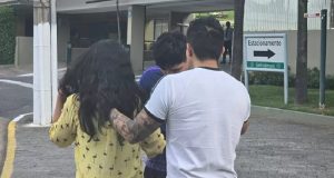 Mulher de roupa amarela cercada por dois homens na rua, de costas