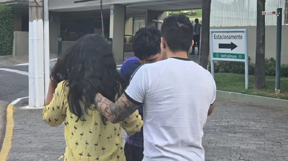 Mulher de roupa amarela cercada por dois homens na rua, de costas
