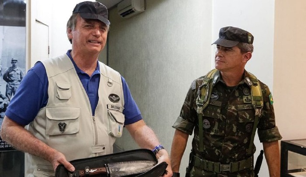 Jair Bolsonaro e o general Mário Fernandes, o primeiro sorrindo e de boné e o segundo sério, olhando para o lado, fardado