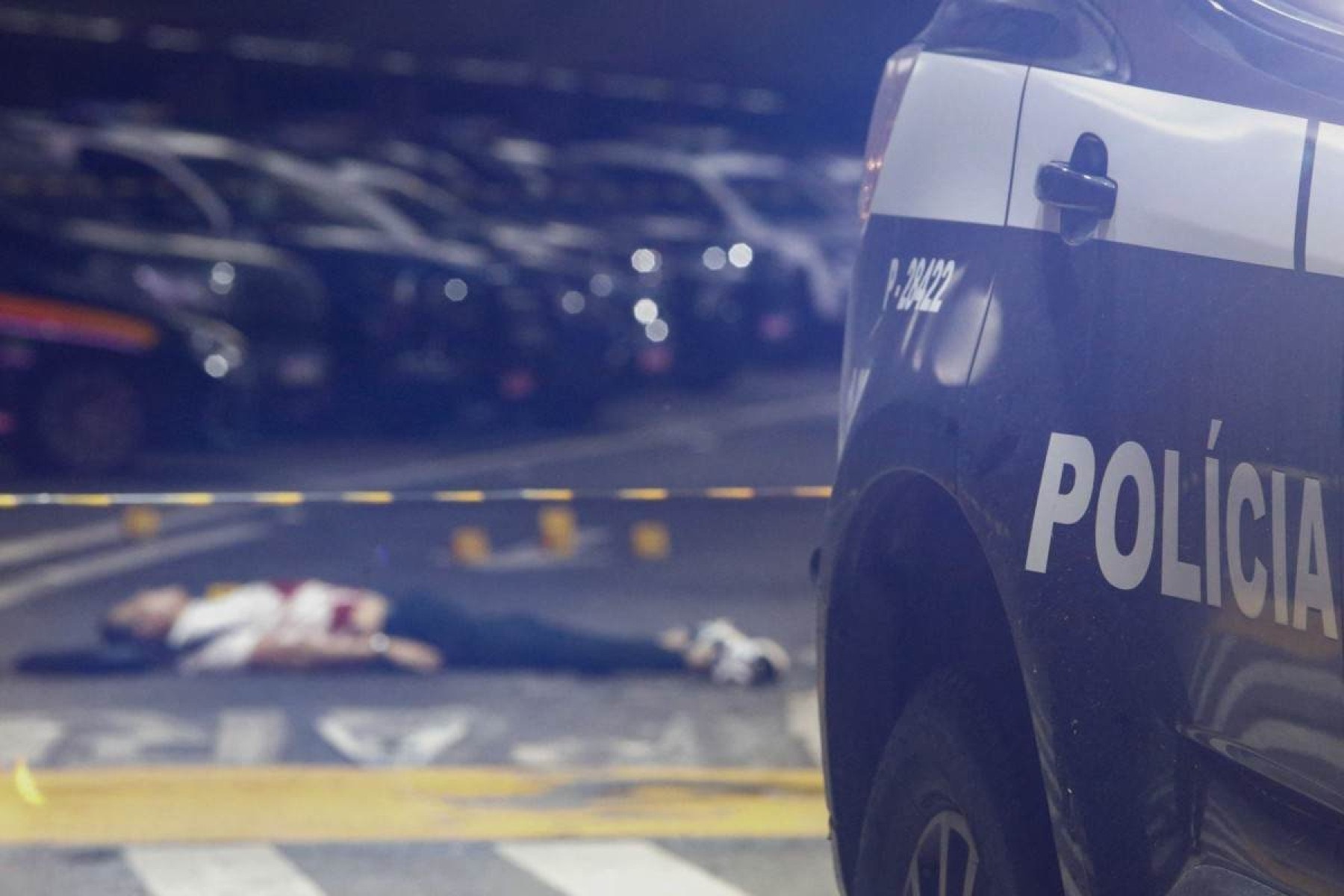 Antônio Vinícius Lopes Gritzbach morto no chão, em segundo plano, com carro da polícia em primeiro plano