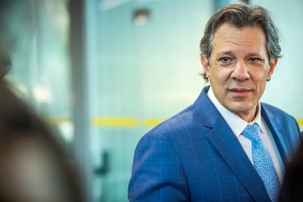 ministro da Fazenda, Fernando Haddad, de terno e gravata azuis, olhando para o lado, sério, sem olhar para a câmera