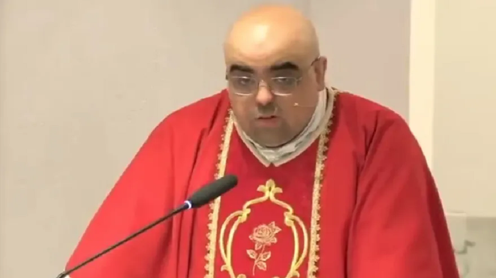 O padre José Eduardo de Oliveira e Silva de batina vermelha falando em microfone, sério