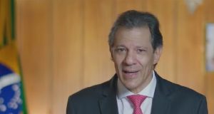 O ministro da Fazenda, Fernando Haddad, falando para a câmera, de terno e gravata, sério