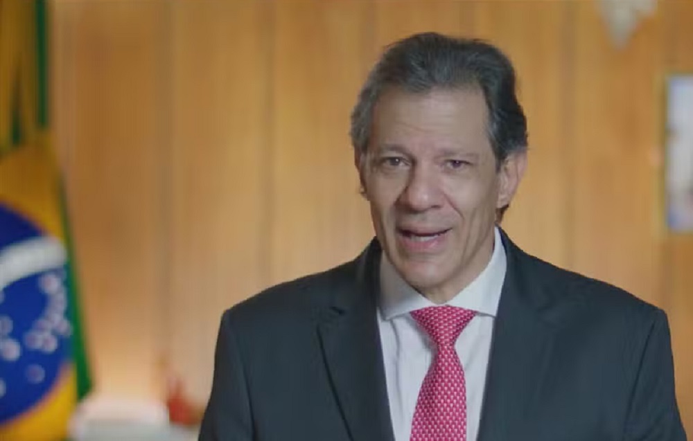 O ministro da Fazenda, Fernando Haddad, falando para a câmera, de terno e gravata, sério