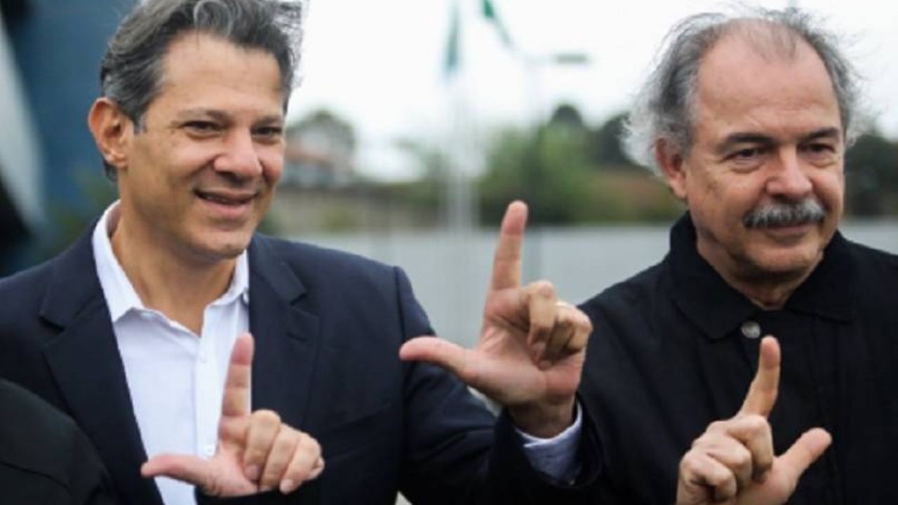 Fernando Haddad e Aloizio Mercadante fazendo o L com as mãos, sem olhar para a câmera
