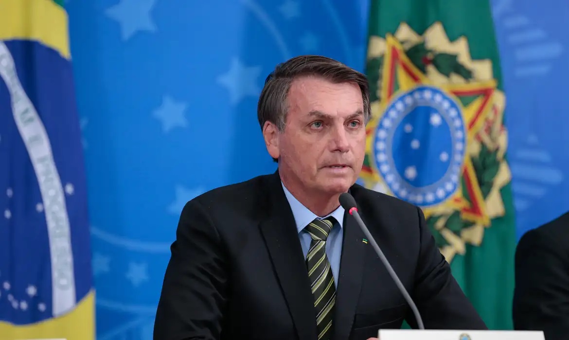 ex-presidente Jair Bolsonaro (PL) com cara de preocupação, perto de bandeiras, sem olhar para a câmera