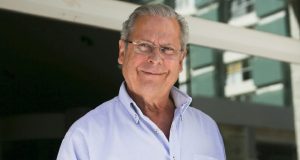 José Dirceu de óculos e camisa social clara, sorrindo de maneira tímida para a câmera