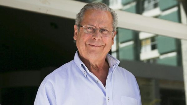 José Dirceu de óculos e camisa social clara, sorrindo de maneira tímida para a câmera