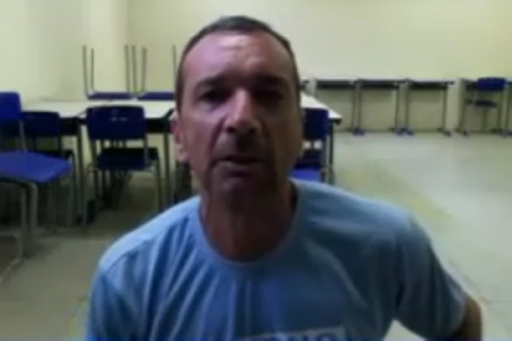Marcos Herbas William Camacho, mais conhecido como Marcola, de camiseta azul, olhando para frente e falando, com cadeiras e mesas atrás