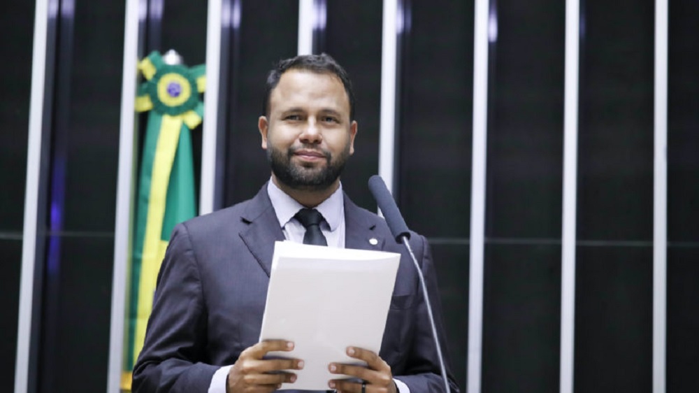 deputado Pastor Henrique Vieira (RJ) sorrindo na Câmara, segurando papel, sem olhar para a câmera, em pé