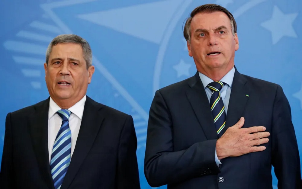 Walter Braga Netto e Jair Bolsonaro em pé, lado a lado, sérios, cantando, sem olhar para a câmera