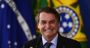 ex-presidente Jair Bolsonaro (PL) rindo e segurando microfone, com bandeiras ao fundo