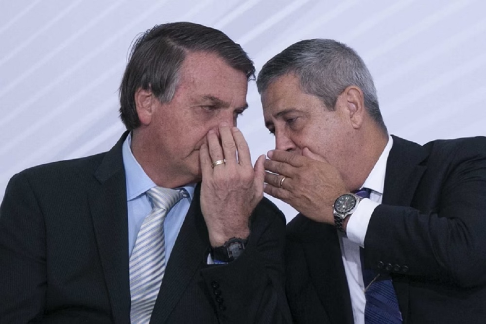 Jair Bolsonaro e general Walter Braga Netto cochichando com mãos na frente da boca e rostos próximos