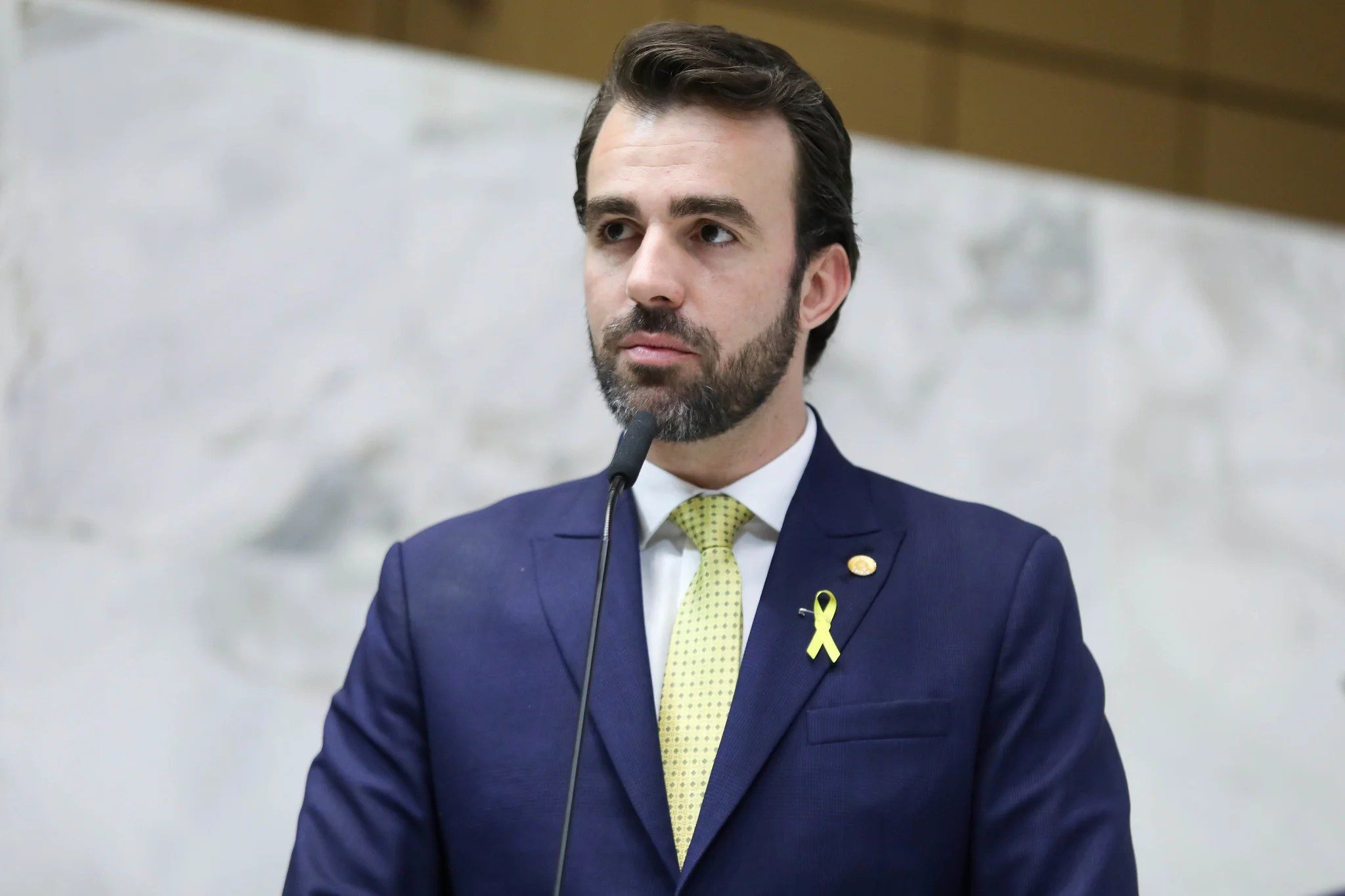 O deputado estadual bolsonarista Lucas Bove (PL) olhando pra frente, sem olhar pra câmera, sério, de roupa social azul marinho