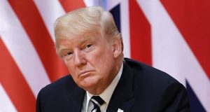 O presidente eleito, Donald Trump, com expressão séria e pensativa e bandeira dos EUA ao fundo