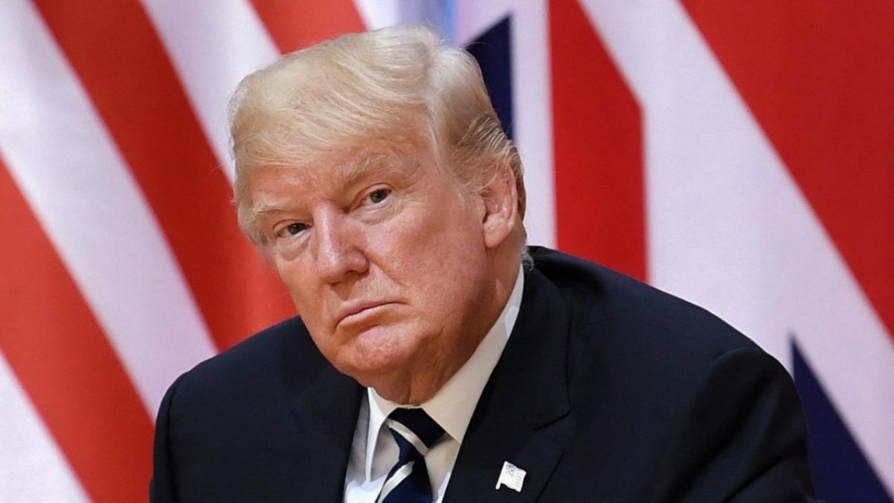 O presidente eleito, Donald Trump, com expressão séria e pensativa e bandeira dos EUA ao fundo
