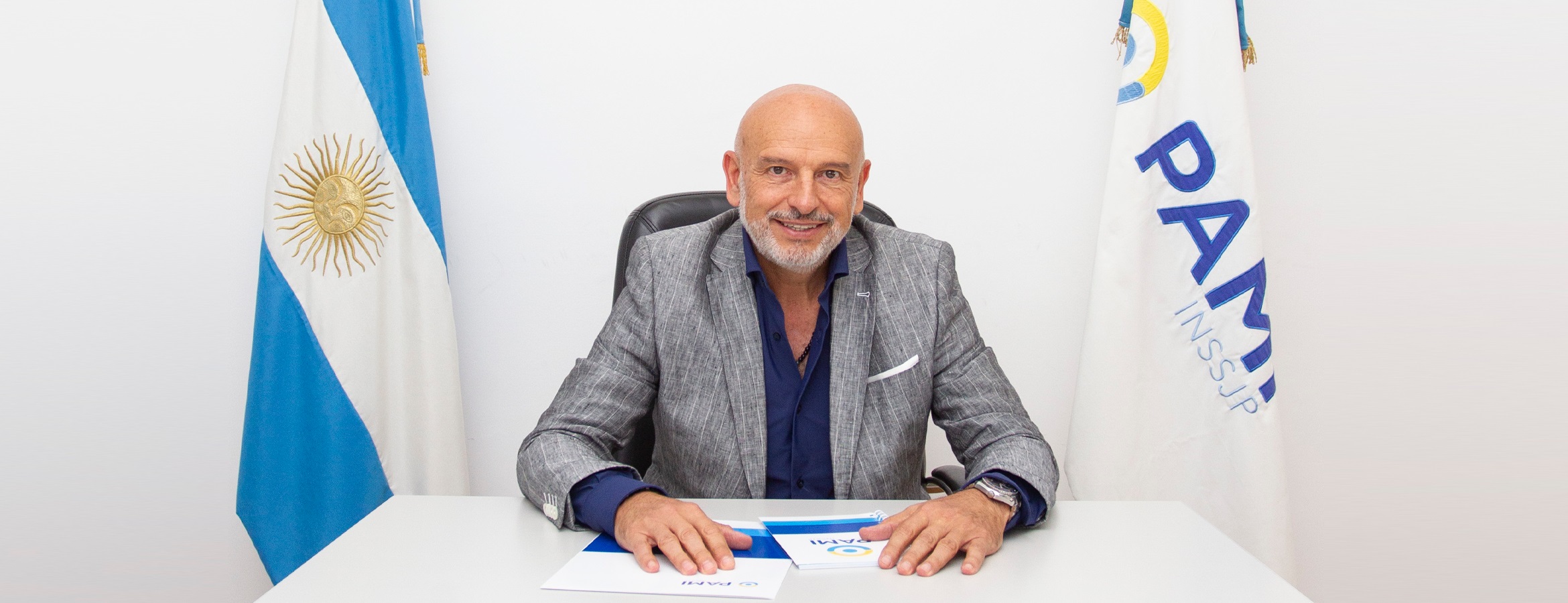 Diretor executivo do PAMI, Esteban Leguizamo, sorrindo, sentado, perto de bandeiras