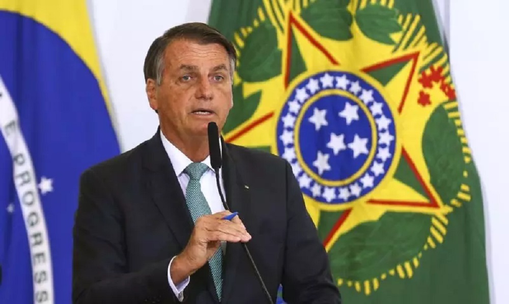ex-presidente Jair Bolsonaro (PL) falando em microfone com bandeiras ao fundo, sério