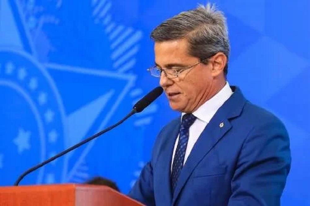 General da reserva Mario Fernandes de perfil e de roupa social azul, falando em microfone, cabisbaixo e sério