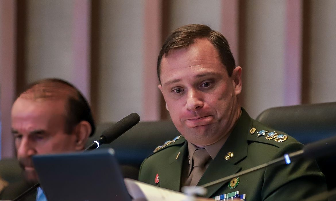 Mauro Cid fardado com expressão de tristeza, sem olhar para a câmera