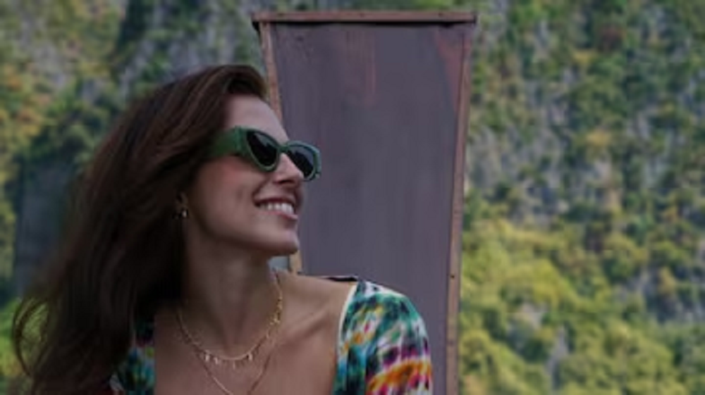 médica Carolina Canales de óculos escuros e cabelo solto, olhando para o lado e sorrindo